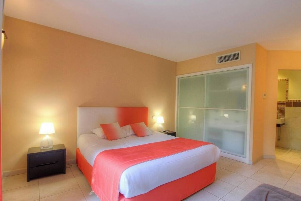Une chambre d’hôtel avec un lit, des tables de chevet, une porte-fenêtre coulissante et une salle de bain visible à travers la porte.