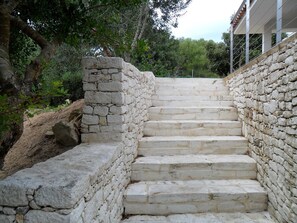 Un escalier en pierre menant au sommet d’une colline, entouré de verdure et d’arbres.