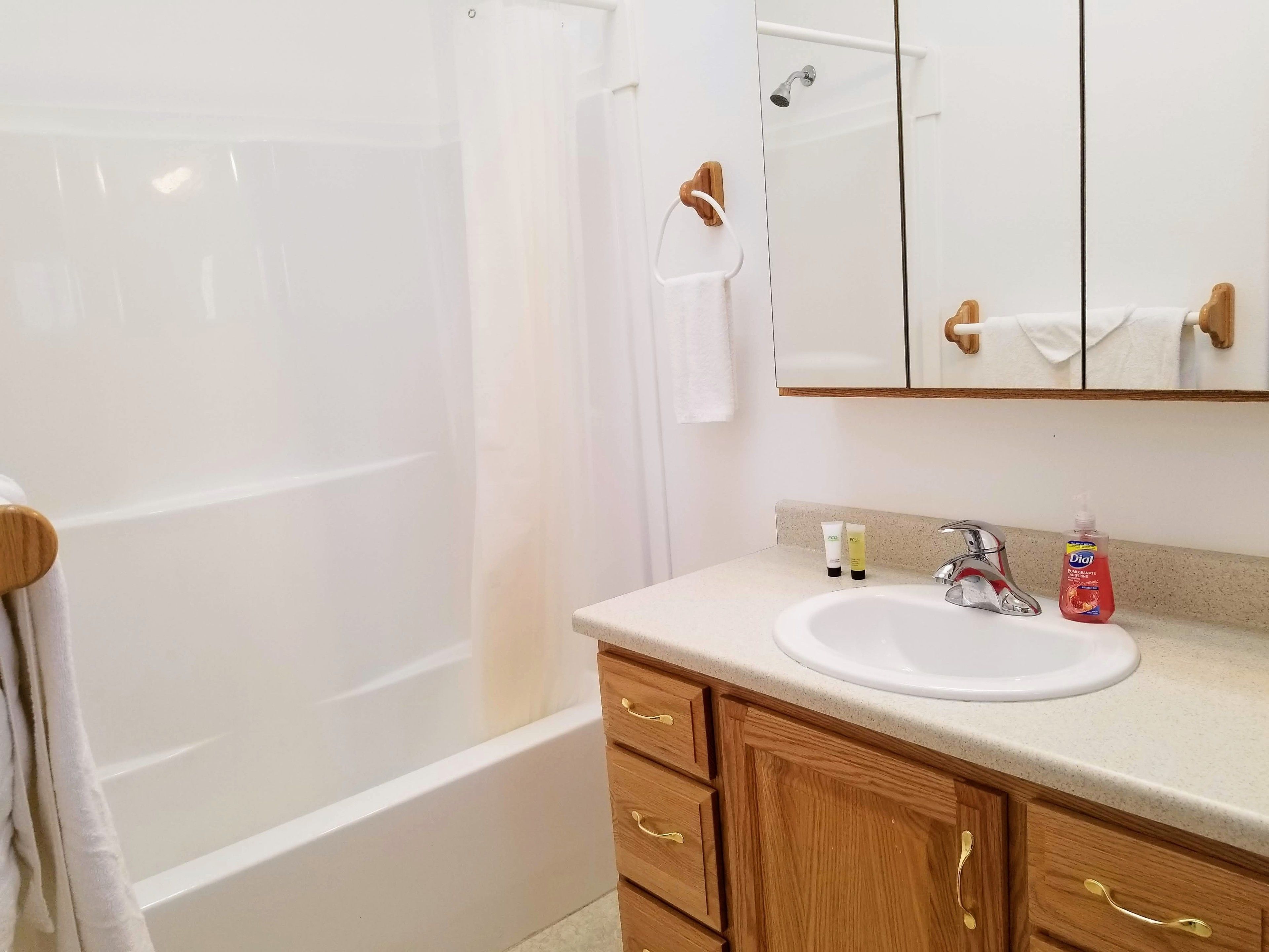 A bathroom with a bathtub, a sink, and a mirror. There are toiletries on the counter.