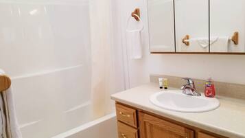 A bathroom with a bathtub, a sink, and a mirror. There are toiletries on the counter.
