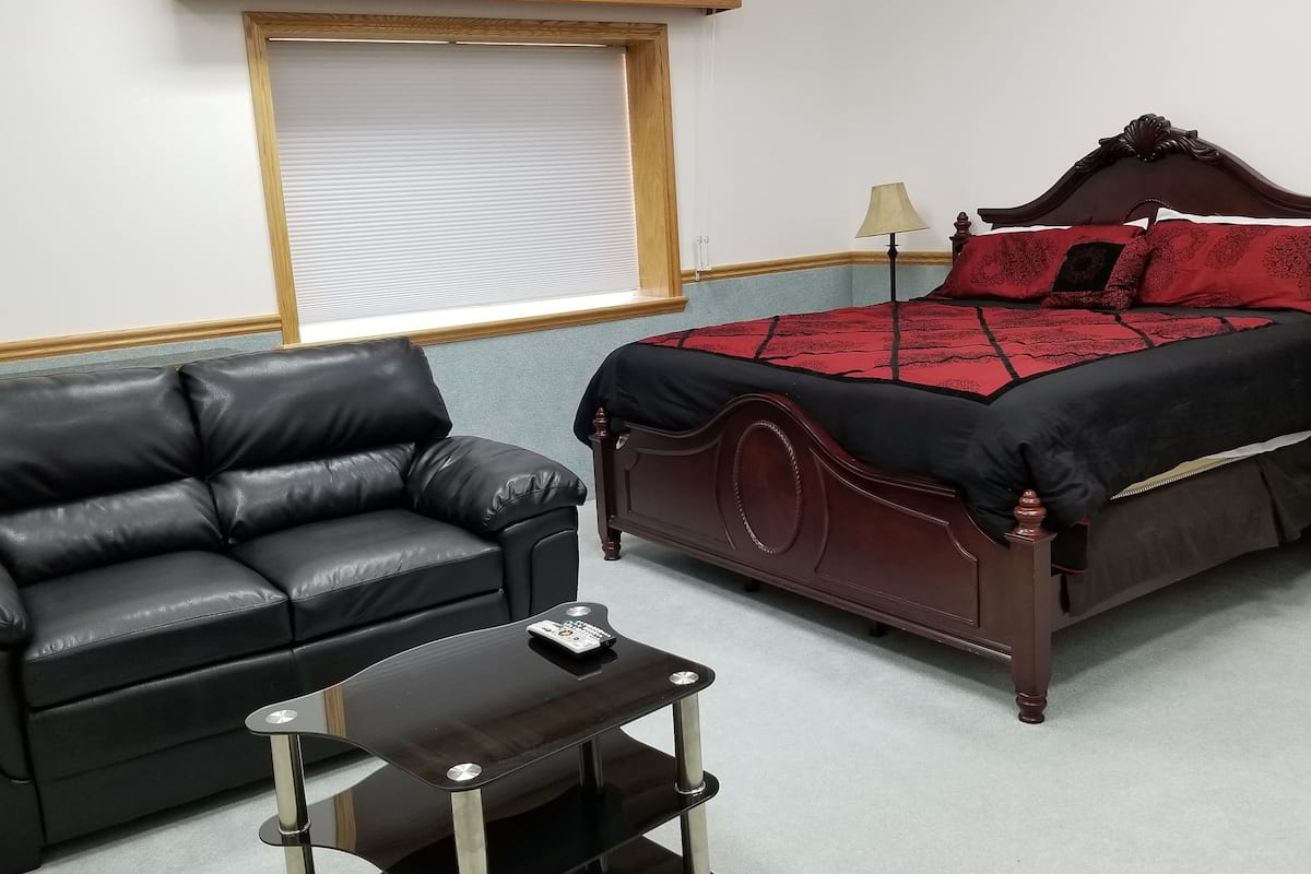 Un dormitorio con una cama de madera oscura, un sofá de cuero negro y una mesita con un control remoto.