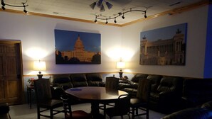 A room with a round table surrounded by leather sofas, two lamps, and two paintings of buildings on the walls. - Zion's Most Wanted Hotel (Hildale)