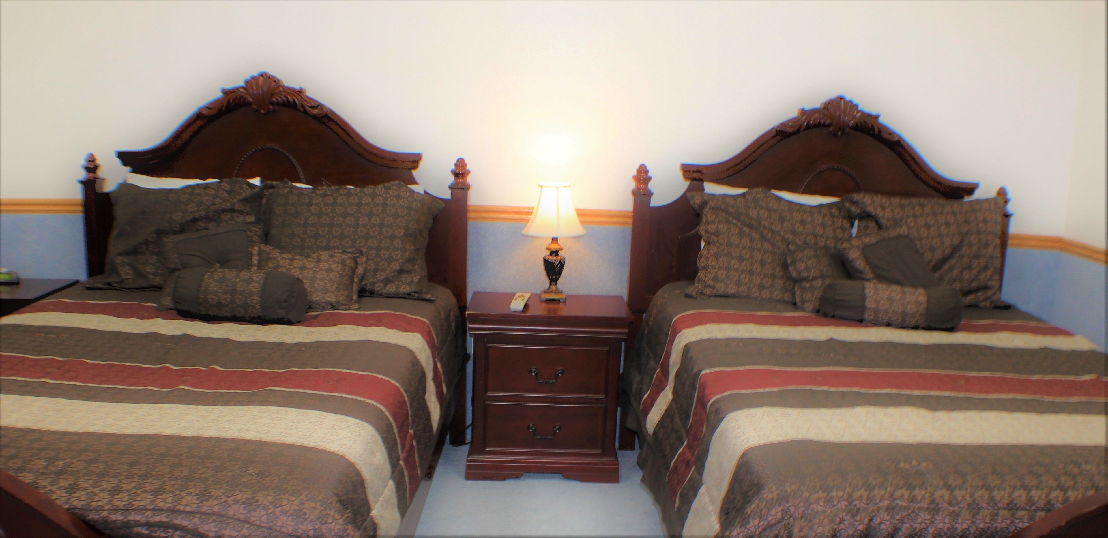 Een hotelkamer met twee houten bedden, elk voorzien van beddengoed met een patroon en kussens. Tussen de bedden staat een nachtkastje met een lamp.