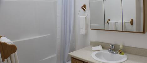A bathroom with a bathtub, a shower curtain, a sink, and a mirror.