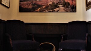 A room with two dark armchairs facing a fireplace, a large painting of a canyon landscape above the fireplace, and a framed picture to the left. - Zion's Most Wanted Hotel (Hildale)