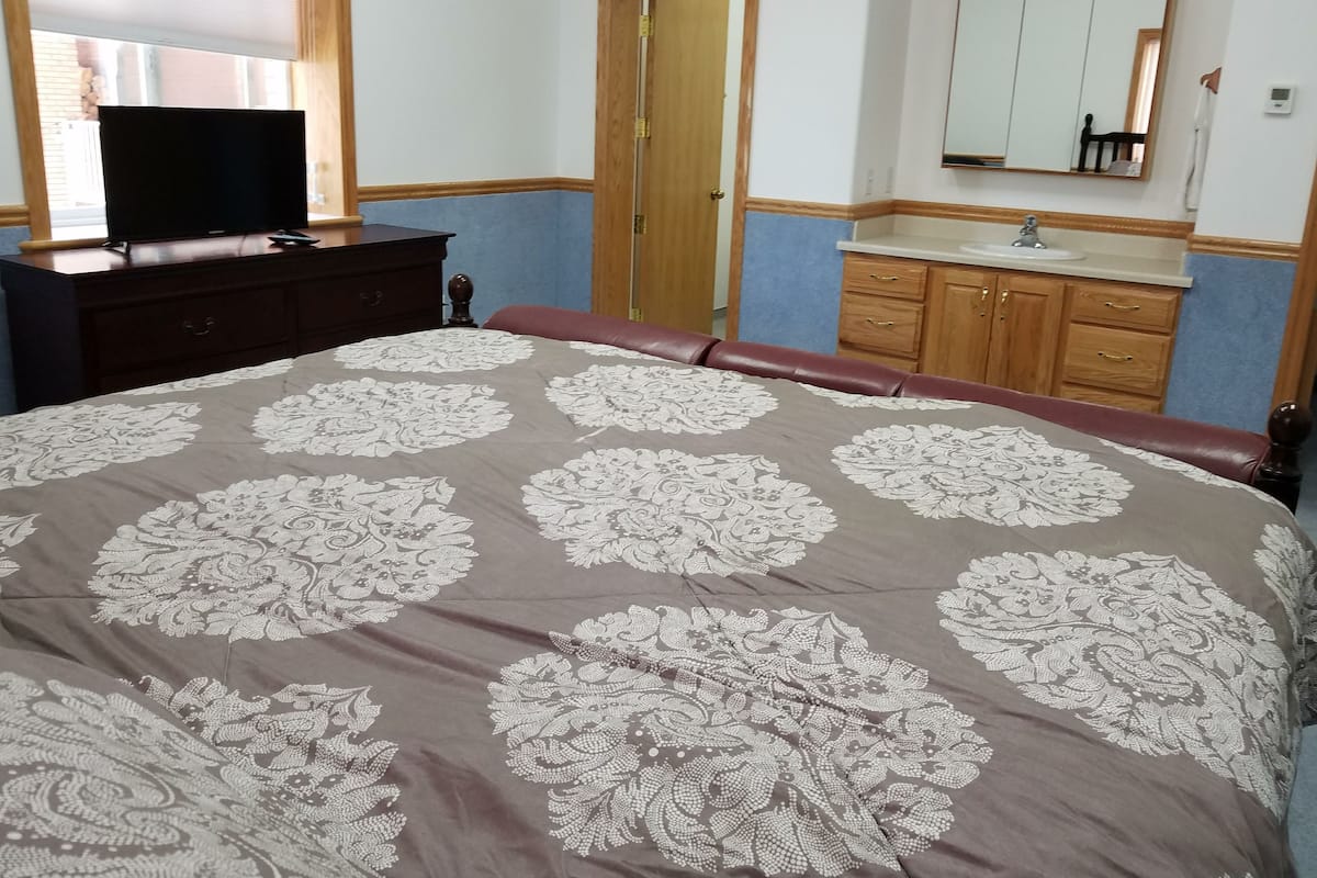 Un dormitorio con una cama grande, un aparador, un tocador con espejo y un televisor sobre un aparador.