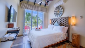 A hotel room with a bed, a desk with a TV, a ceiling fan, and a view of palm trees. - Brisa Oceano Resort (Placencia)
