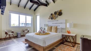 A hotel room with a large bed, a ceiling fan, a window with a view, a small table with a lamp, and a trash can.