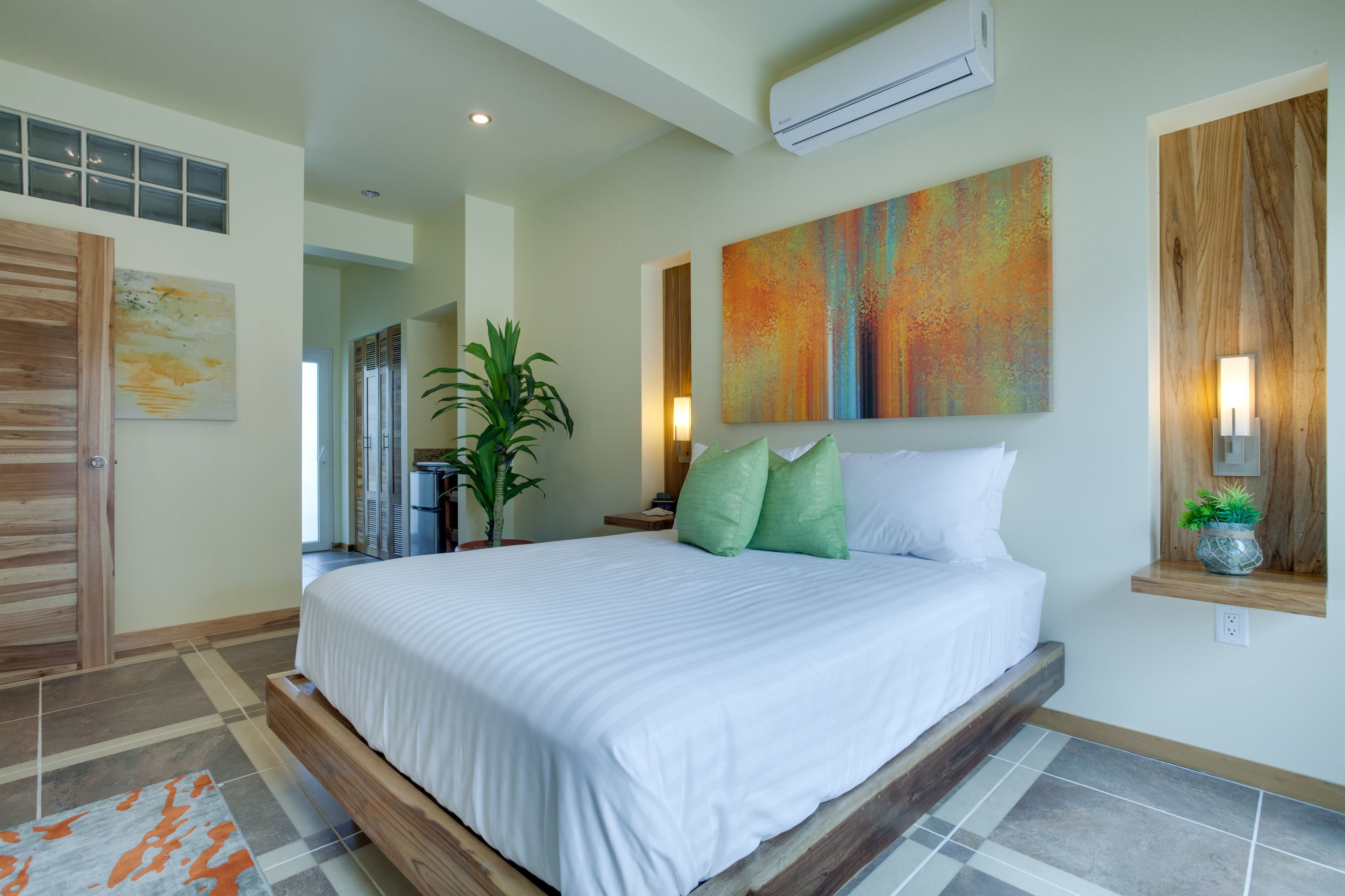 Un dormitorio moderno con una cama grande, una planta en maceta y un cuadro abstracto colorido.