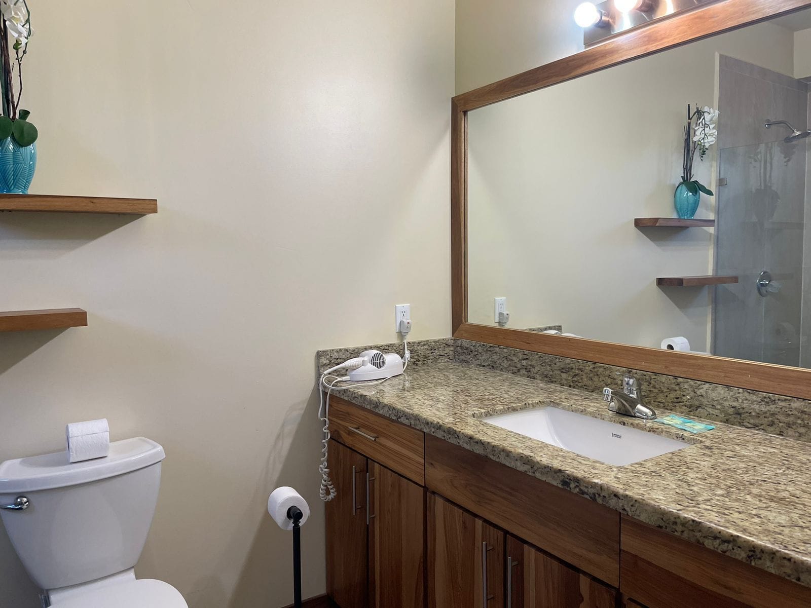 A bathroom with a granite countertop sink, wooden cabinets, a toilet, and a mirror.