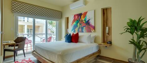 A bedroom with a bed, a desk, a chair, a potted plant, and a colorful abstract painting on the wall.
