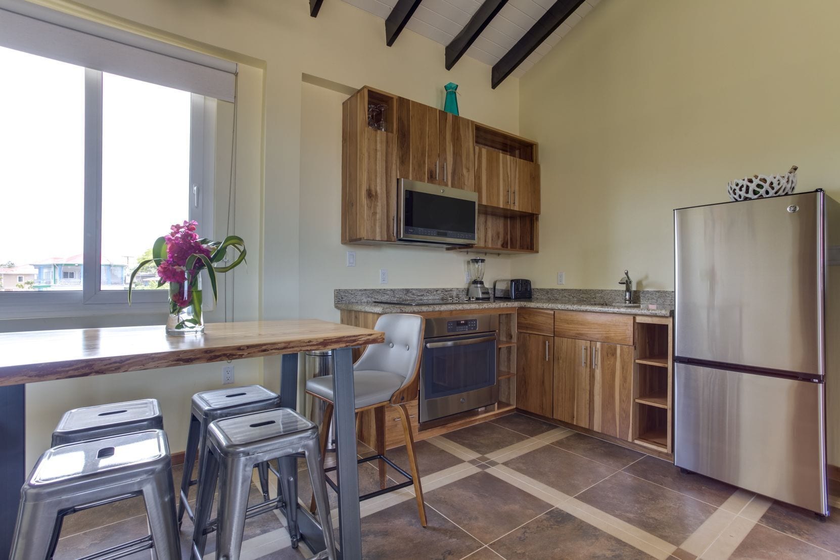A modern kitchen with wooden cabinets, a stainless steel refrigerator, a built-in oven, and a granite countertop.