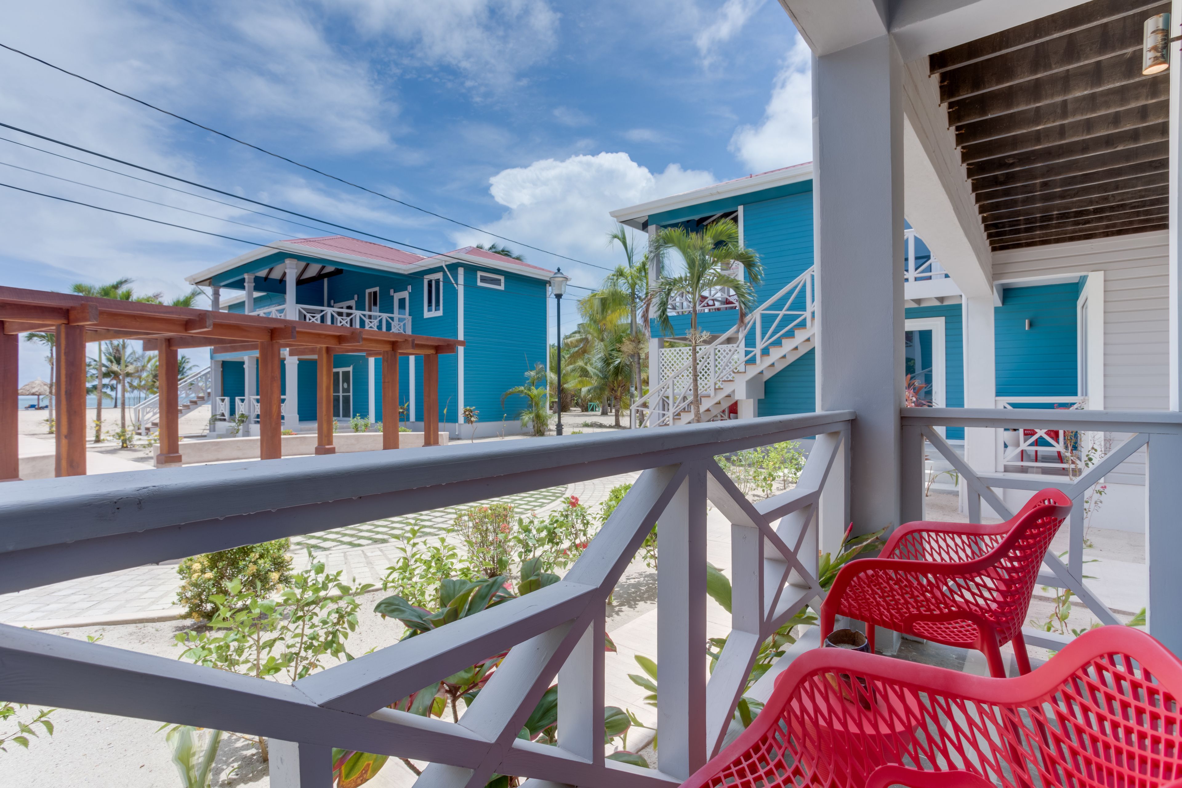 A balcony with a white railing, red chairs, and a view of two blue buildings with white trim.