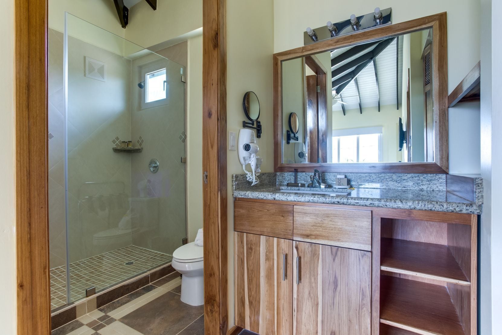Un baño con cabina de ducha de vidrio, inodoro, tocador con espejo y lavamanos.