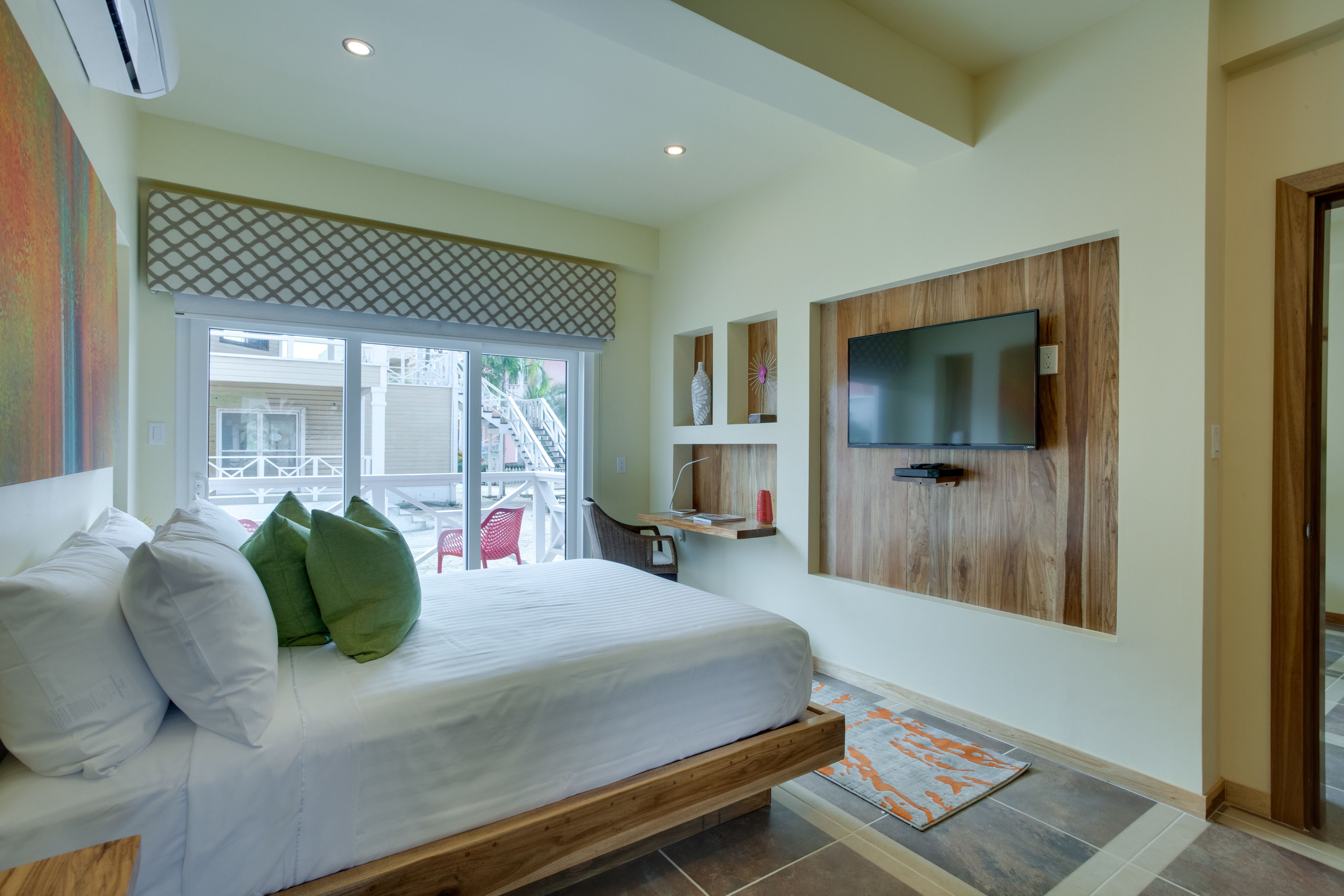 Een slaapkamer met een bed, een aan de muur bevestigde televisie en uitzicht op buiten.