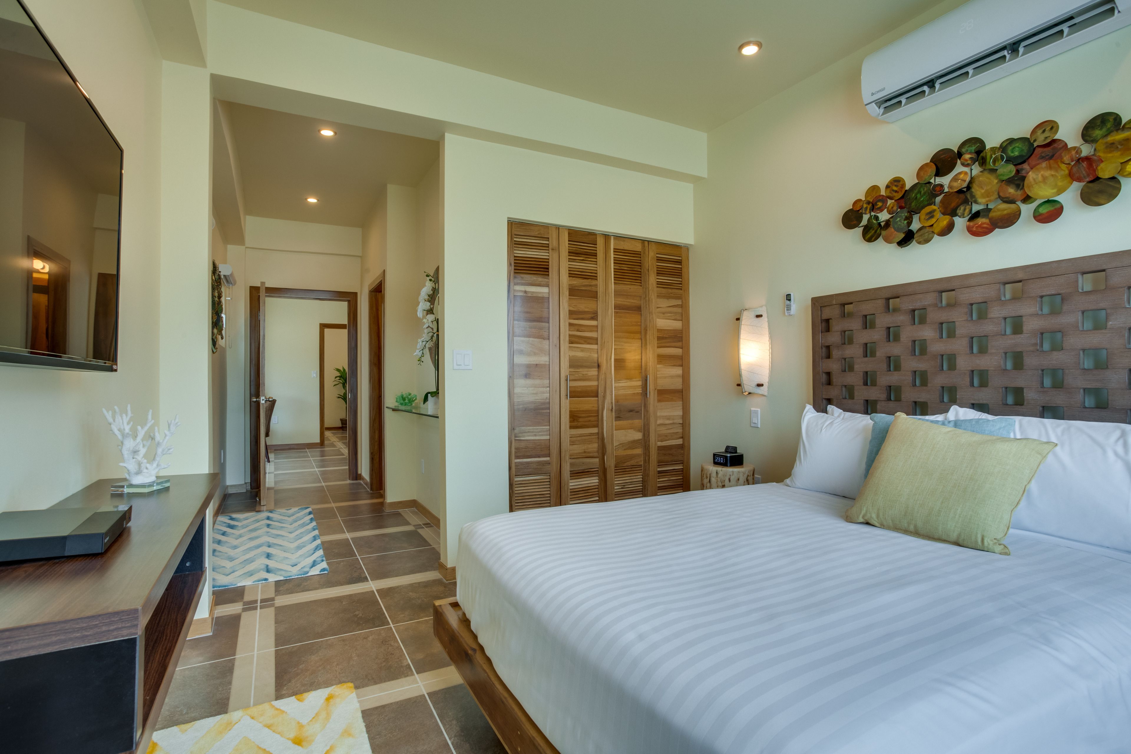 Una habitación de hotel con una cama, cabecera de madera, aire acondicionado instalado en la pared y un adorno mural.