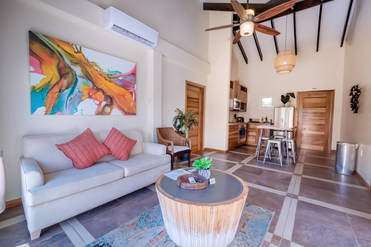 A modern living room with a white sofa, a round wooden coffee table, and a colorful abstract painting.