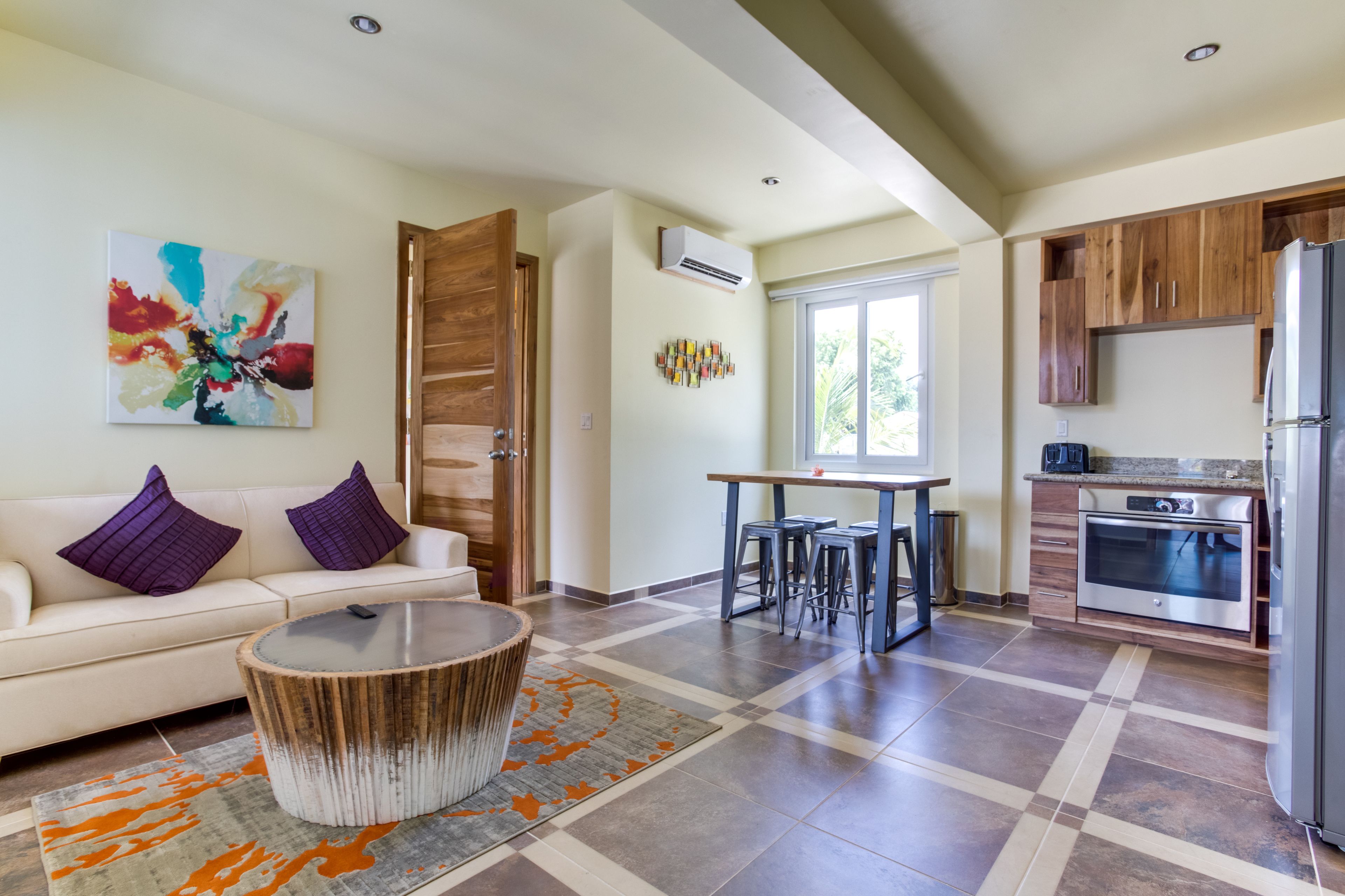 A modern kitchen with a dining area, a sofa with purple cushions, and a coffee machine.