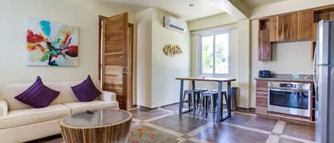 A modern kitchen with a dining area, a sofa with purple cushions, and a coffee machine.