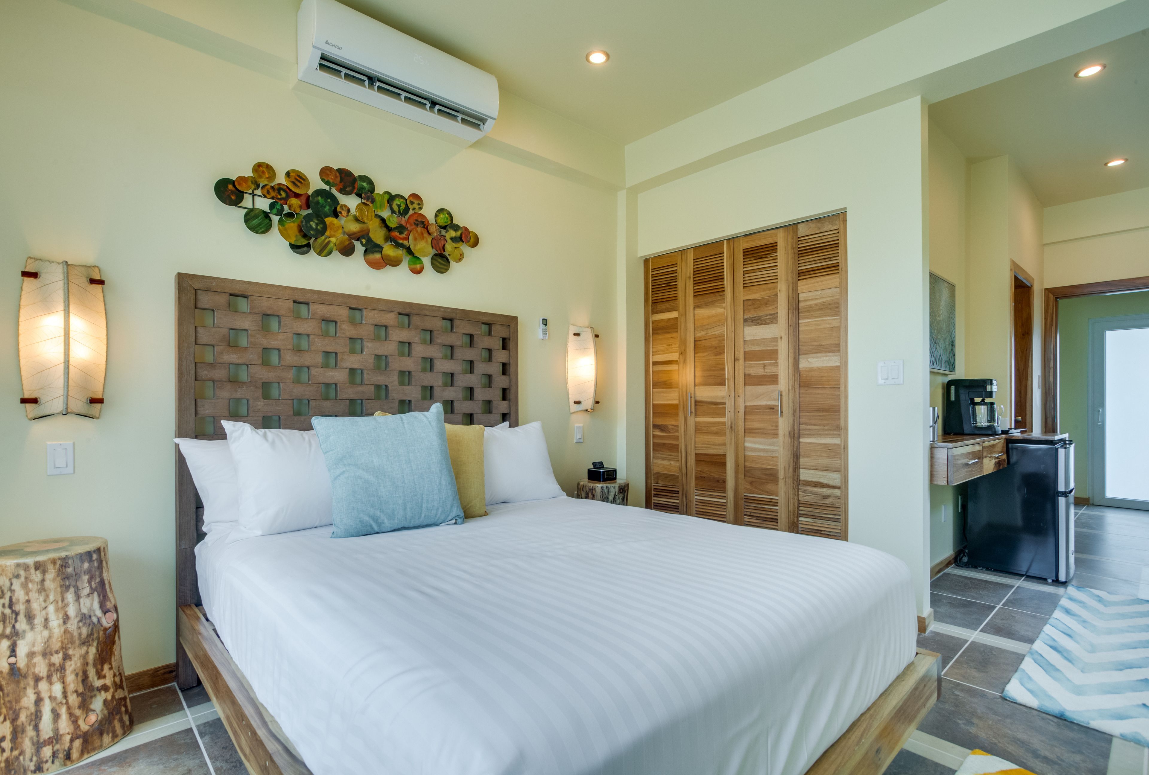 A hotel room with a large bed, wooden headboard, wall-mounted artwork, and a kitchenette.