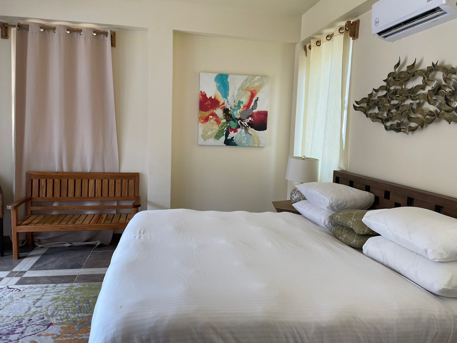Ein Hotelzimmer mit einem großen Bett, einer Holzbank, einem farbenfrohen abstrakten Gemälde und einem dekorativen Wandbild.