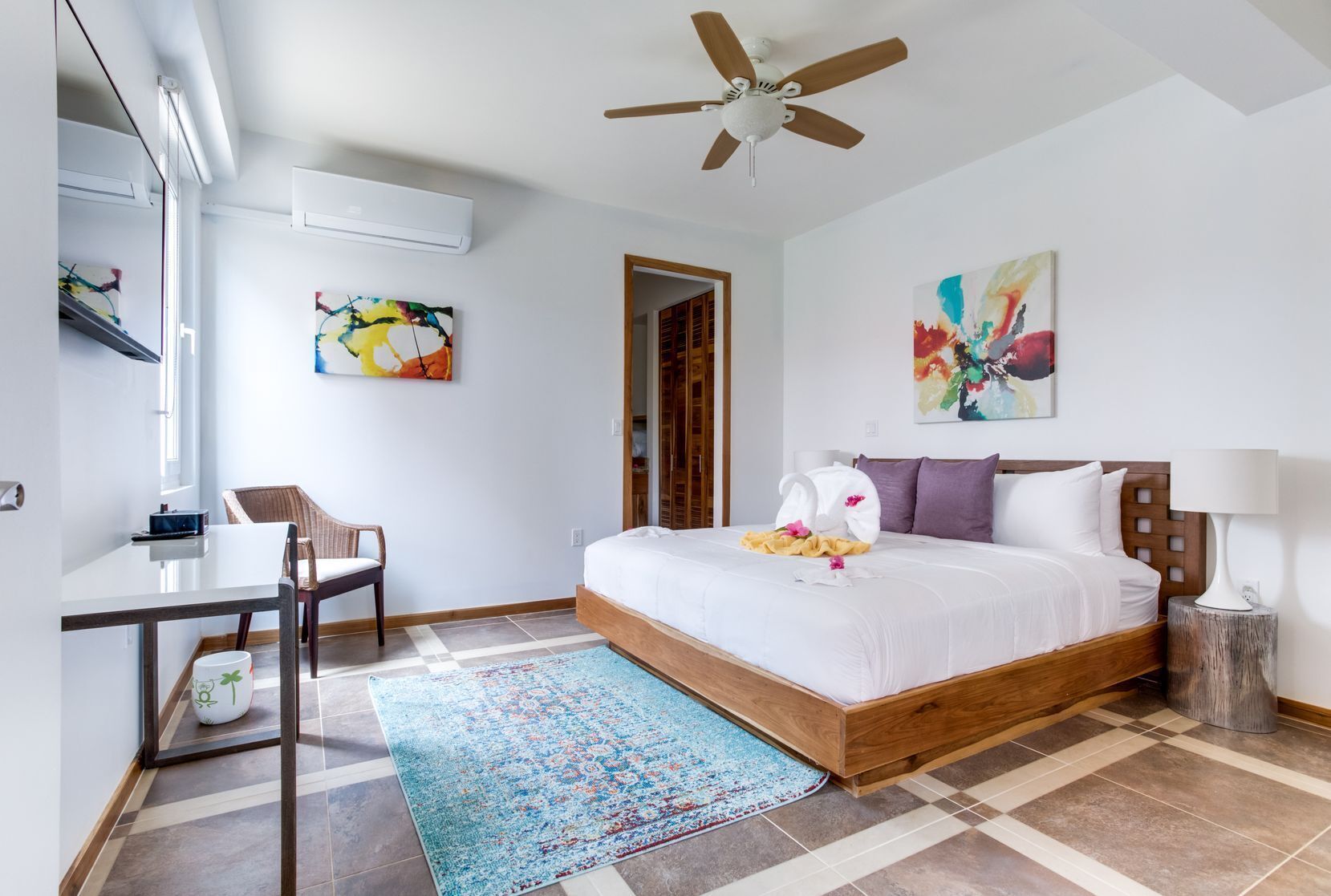 A modern hotel room with a large bed, a desk, a chair, and a ceiling fan.