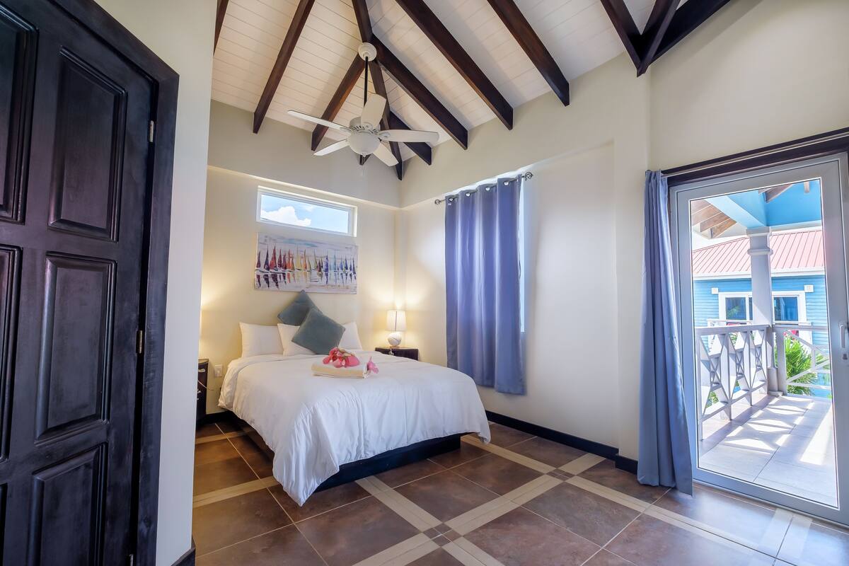 A bedroom with a bed, a ceiling fan, a window with curtains, and a view of the outside balcony.