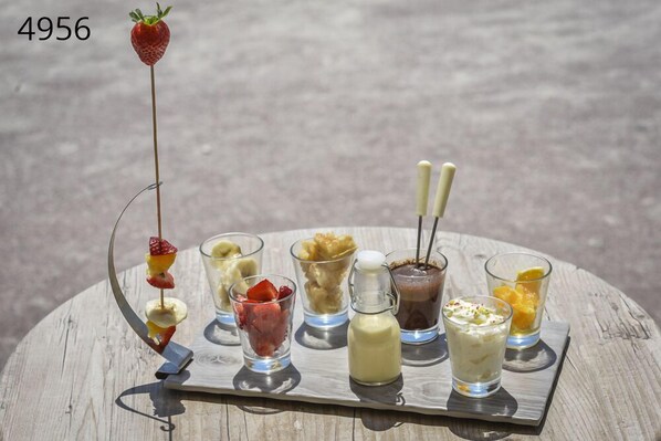 A tray with various food items including a strawberry skewer, fruit cups, and small bottles of sauces.