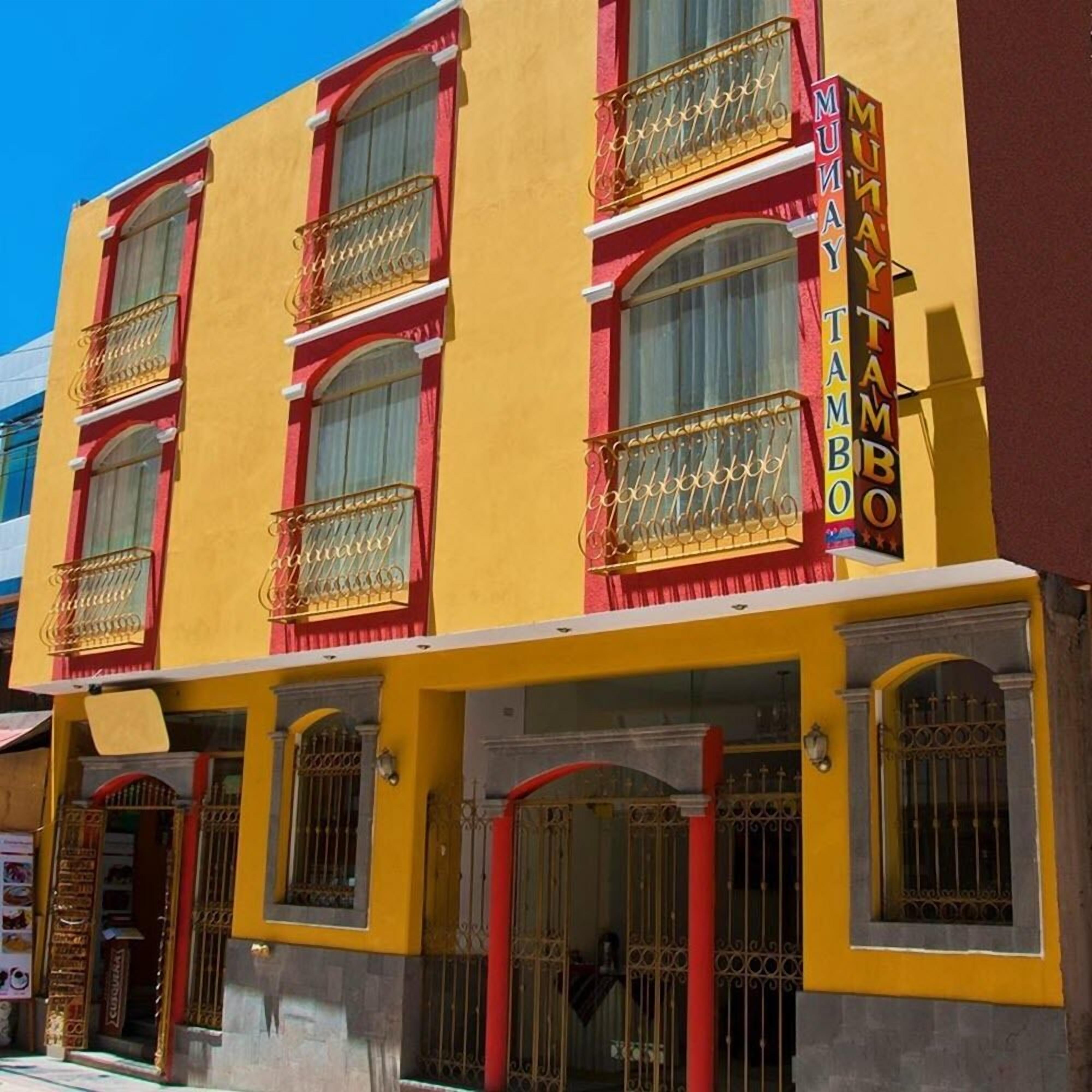 Un edificio amarillo con detalles en rojo y un letrero que dice "MUNAY TAMBO".