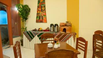 A dining area with a table set for two, a potted plant, and a painting on the wall.