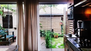 Una cocina con cafetera, una mesa de madera y vista a un jardín con valla y plantas.
