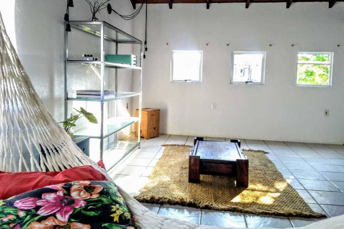 Ein Zimmer mit einer Hängematte, einem Holzbett, einem Glastageslichtschrank und einem kleinen Tisch.