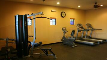 Un gimnasio con equipo de ejercicio, cintas de correr y un reloj en la pared.