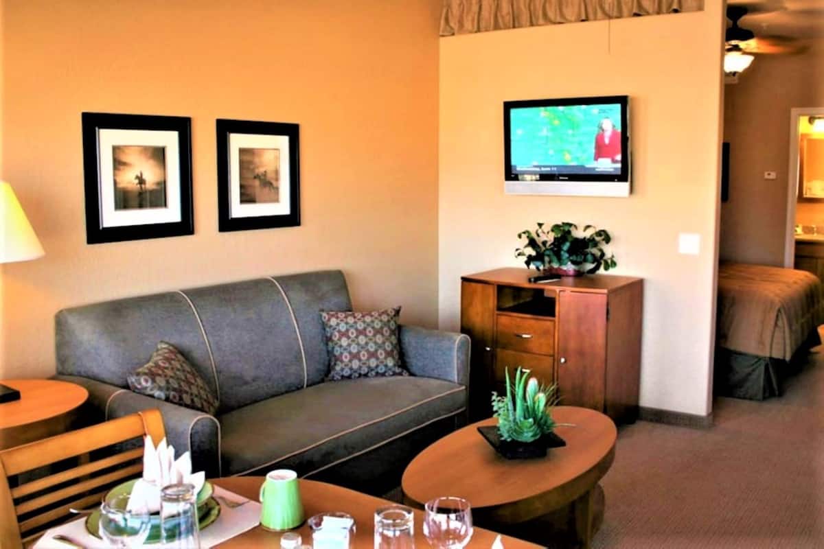 A hotel room with a sofa, a coffee table, a TV mounted on the wall, and a bed in the background.