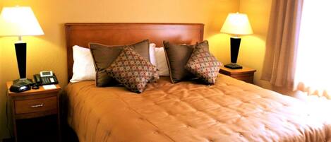 A hotel room with a large bed, two bedside tables with lamps, a telephone, and a nightstand.