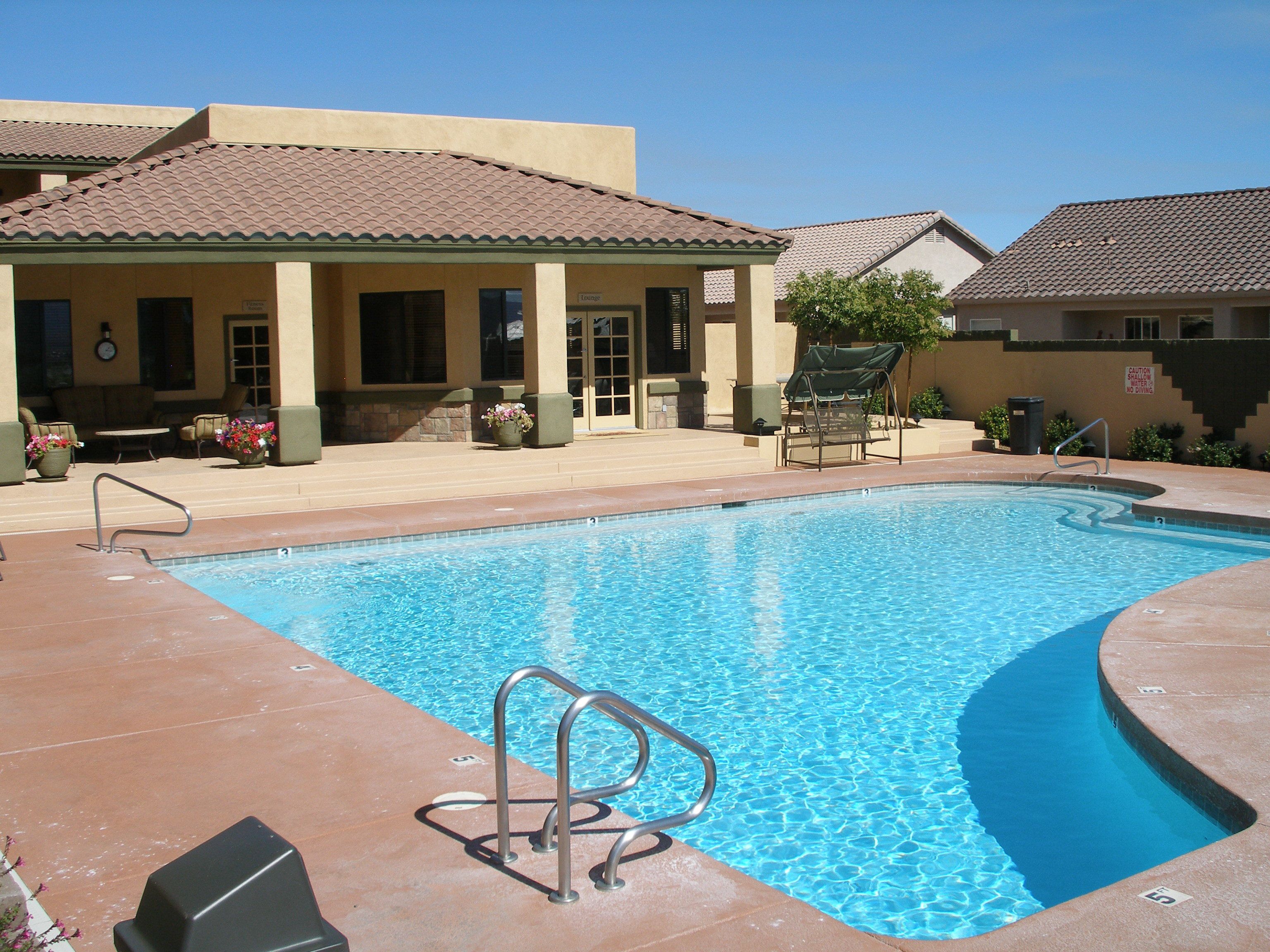 A swimming pool with a metal ladder, outdoor seating, and a building with a tiled roof.