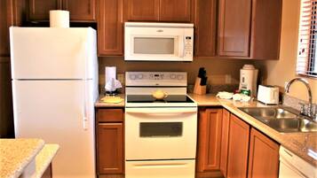 A compact kitchen with a refrigerator, microwave, stove, and sink.