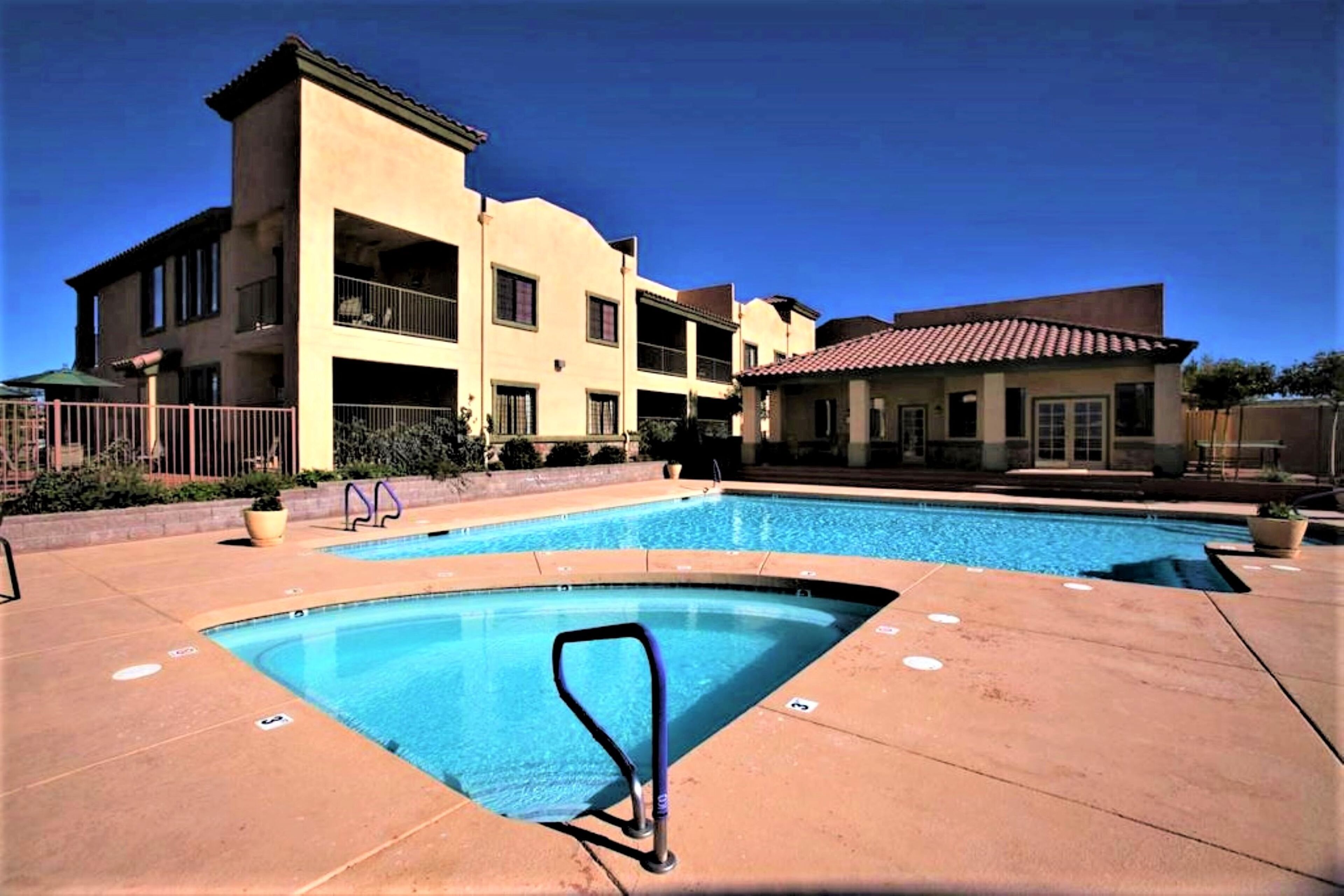 Zona de piscina con una piscina azul cristalina, una escalera para la piscina y un edificio con balcones al fondo.