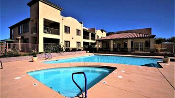 A swimming pool area with a clear blue pool, a pool ladder, and a building with balconies in the background.