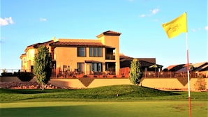 Um edifício grande e de vários andares, com uma bandeira em destaque em um mastro, localizado em um campo de golfe bem cuidado.
