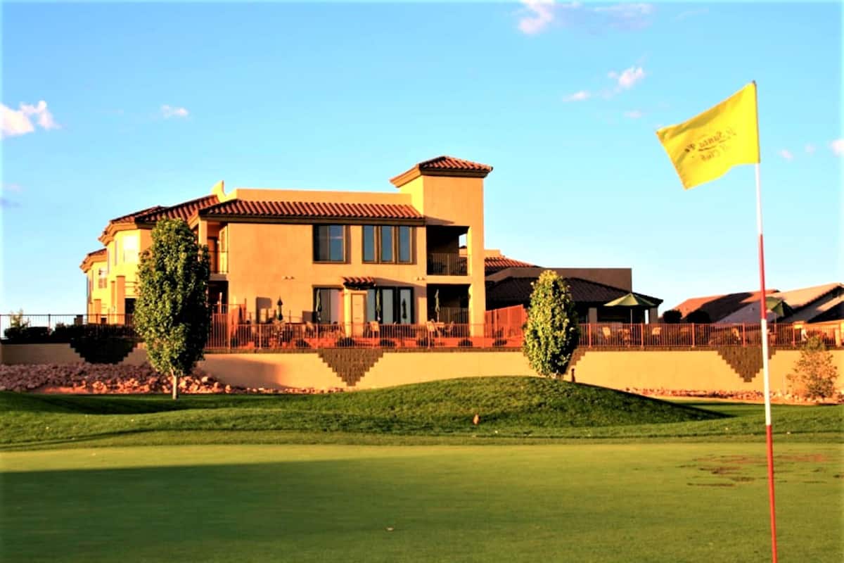 A large, multi-story building with a prominent flag on a flagpole, situated on a well-maintained golf course.