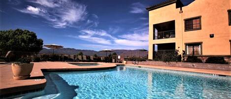 A swimming pool with clear blue water, surrounded by a building with balconies and a mountain backdrop.