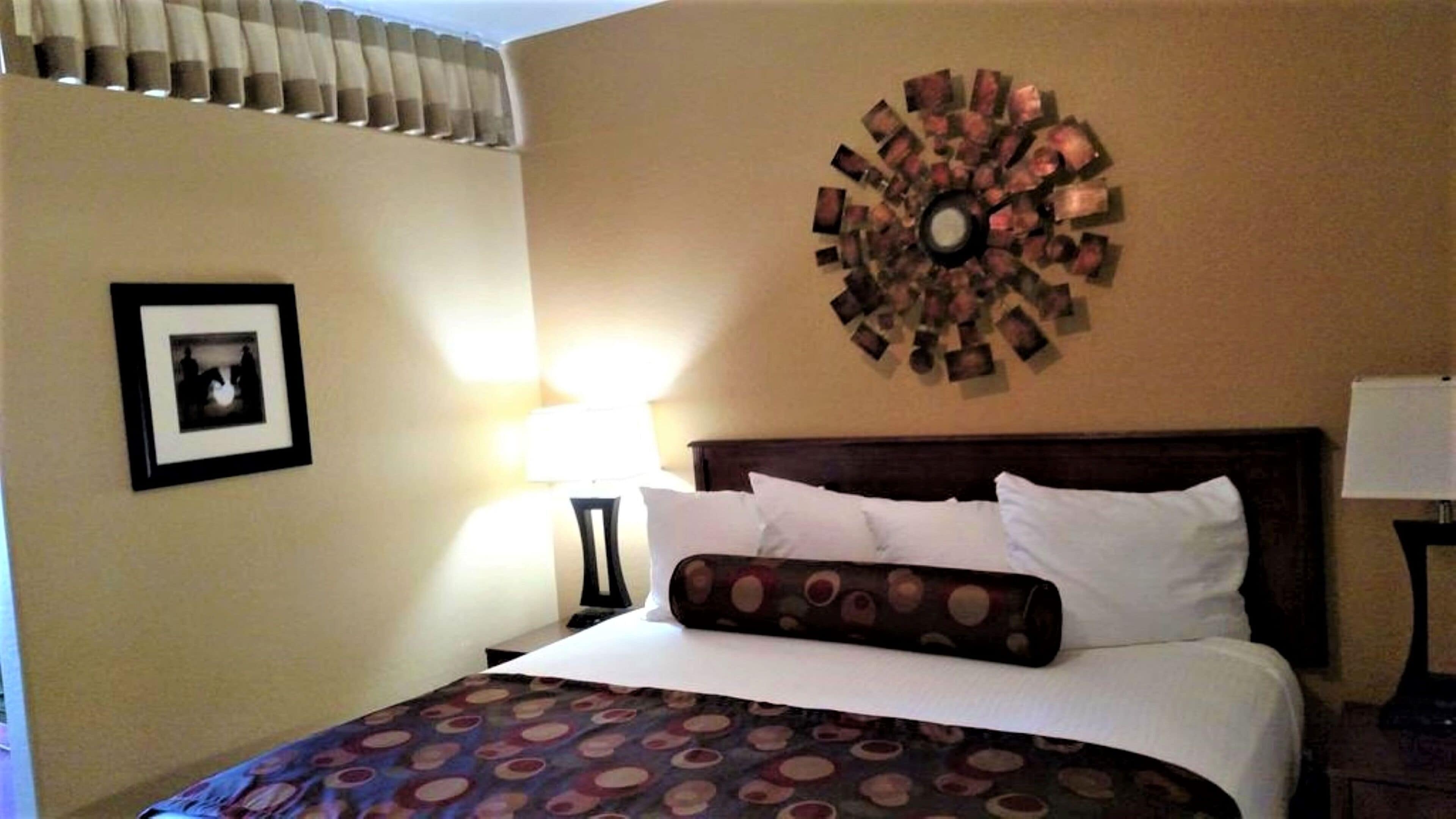 Een hotelkamer met een bed, een ronde wanddecoratie, een ingelijst beeld en een lamp.
