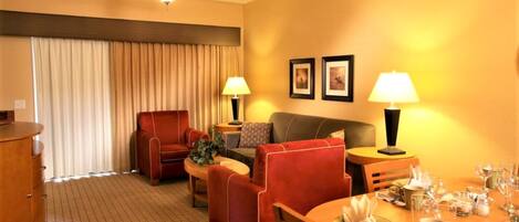 A hotel room with a dining area, a sofa, a chair, a table set for dining, and a ceiling fan.