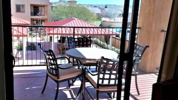 Een balkon met een ronde tafel en vier stoelen, met uitzicht op een woongebied met huizen en een gebouw met een rood dak.