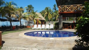 Un espace piscine avec des chaises longues, une terrasse en pierre et des palmiers.