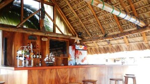 Un bar en bois avec des tabourets, un toit de chaume et une vue sur la mer.
