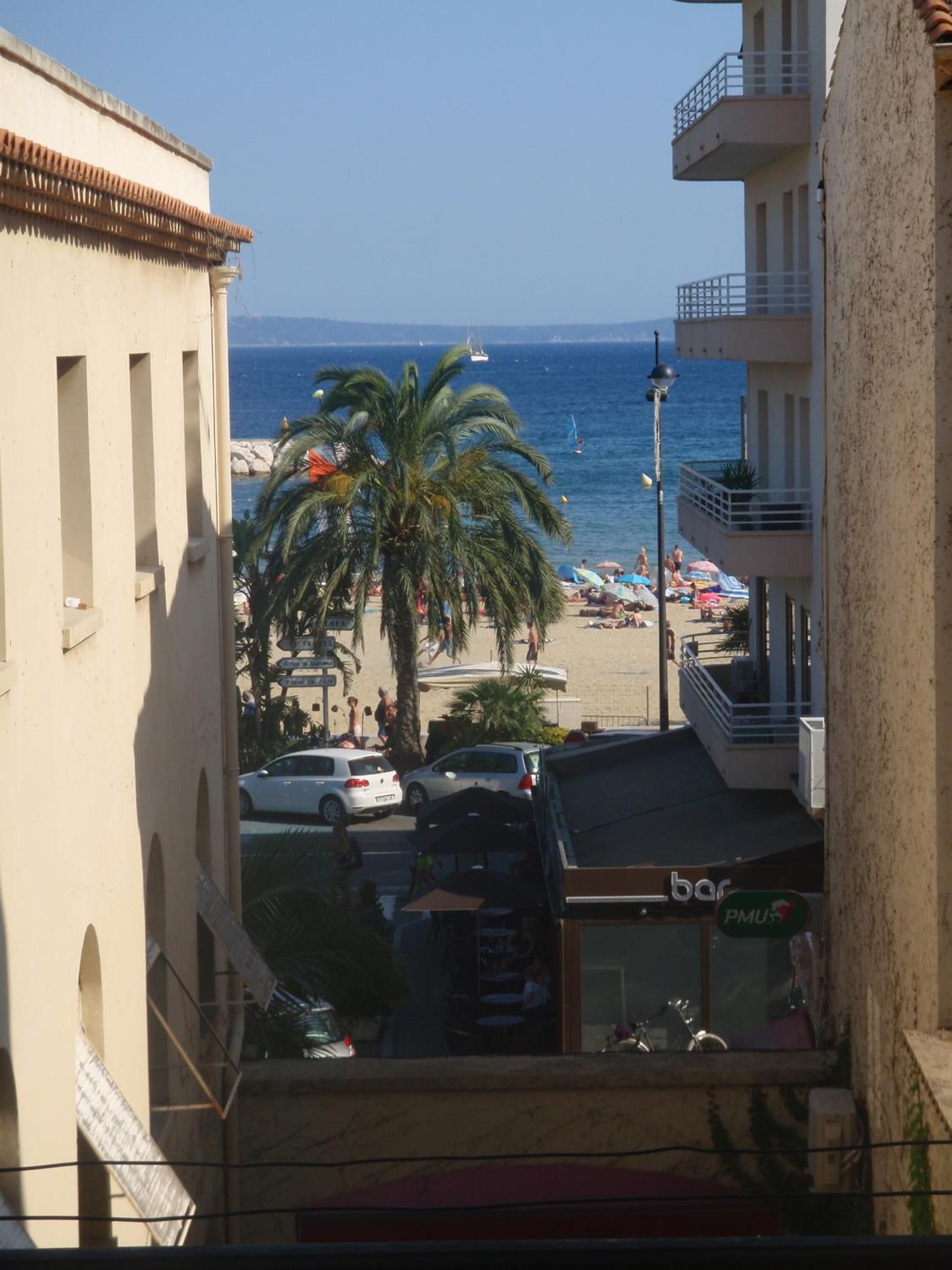 Une vue d’une plage avec des palmiers, des gens et des voitures garées.