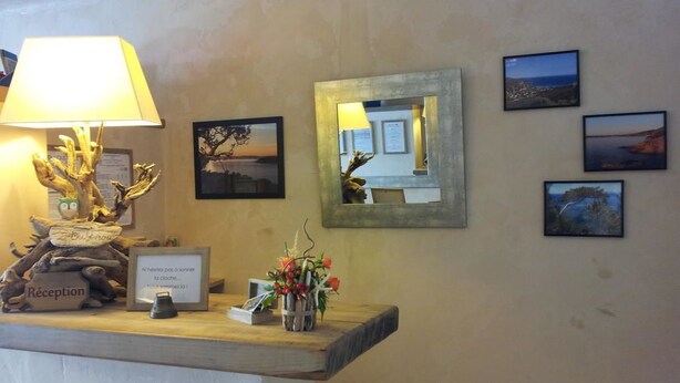 A reception desk with a lamp, a sign, and a framed mirror. - Hôtel L'Oustaou (Le Lavandou)