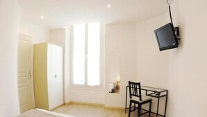 A room with two beds, a desk, a chair, a television, and a window. - Hôtel L'Oustaou (Le Lavandou)